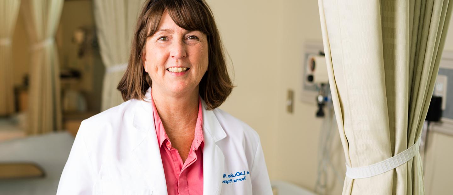 woman in a white lab coat standing in a hospital room by a curtain